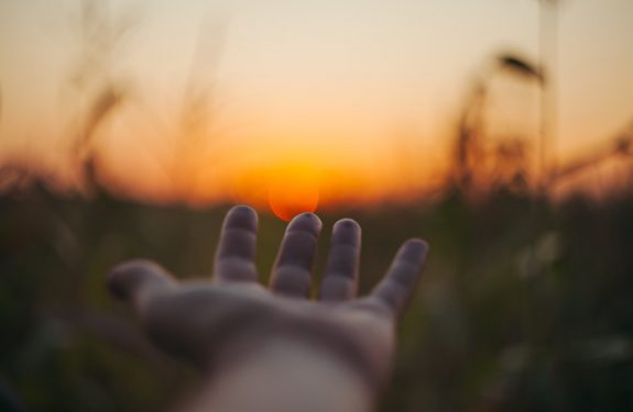 selective focus photo of person laying hand over the sunset