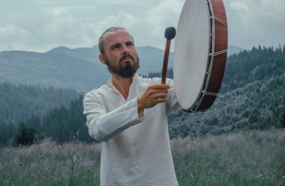 man playing percussion instrument on grass field near forest